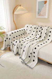 Detail of thick knitted fabric with black grid pattern and white fringe tassel decor