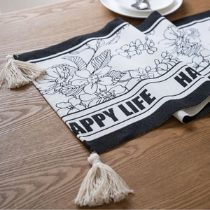 Floral jacquard table runner with black and white patterns and elegant cream tassels
