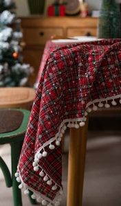 Detail van rood geruit kersttafelkleed met sneeuwvlokkenprint en witte pompons rand