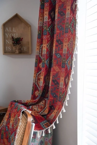 Detailed view of red bohemian woven curtain with ethnic patterns and white tassels