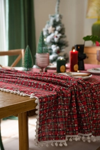 Detail van rood-groene kersttafelloper met sneeuwvlokkenprint en witte pompon-afwerking