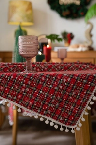 Detail van rood geruit kersttafelkleed met sneeuwvlokken en witte pompons aan de rand