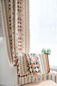 Close-up of bohemian jacquard curtain with geometric patterns and white tassels on wood chair