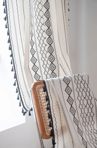 Close-up of bohemian linen curtain with black geometric patterns and handmade tassels