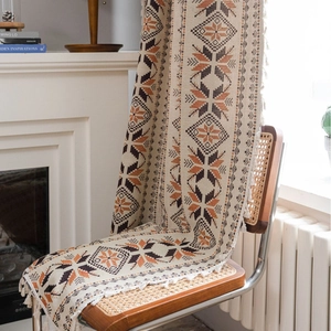 Bohemian geometric woven throw blanket with fringe hanging on a vintage chair