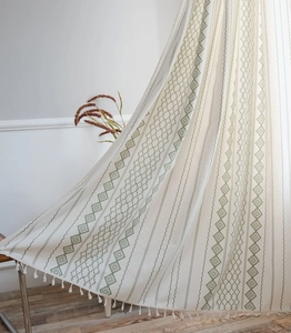 Close-up of bohemian green geometric print on beige linen curtain with white tassels