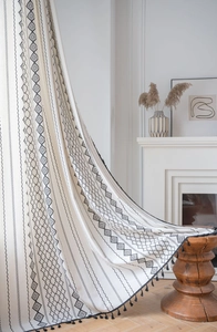 Close-up of bohemian linen curtain with black geometric diamond patterns and tassel trim