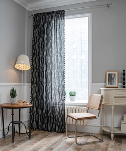 Close-up of black sheer curtain featuring white floral embroidery and tassel fringe details