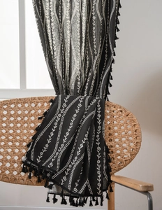 Detail view of black floral fabric with elegant tassels draped on a wicker chair