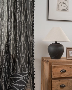 Detail of black curtain featuring white wave floral embroidery and decorative tassel fringe