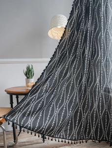 Detail view of black curtain with white vine print and side tassels in a cozy room