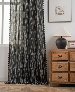 Detail of bohemian black curtain with white floral vines and textured fringe tassels