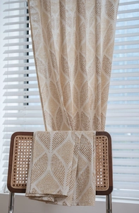 Détail d'un rideau aspect lin avec motif de feuilles marron drapé sur une chaise en rotin
