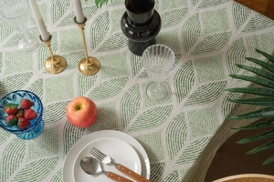 Detail of beige cotton linen tablecloth with green geometric leaf prints in a cozy dining set