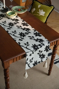 Close-up of black and white floral pattern table runner with creamy beige fringe tassels