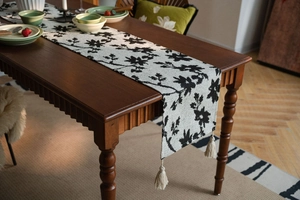 Detail of Nordic floral table runner with elegant tassels on a dark wood dining table
