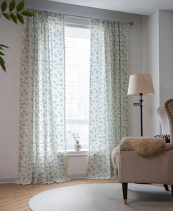 Vue détaillée des rideaux floraux bleus avec d'élégants pompons blancs et texture du tissu