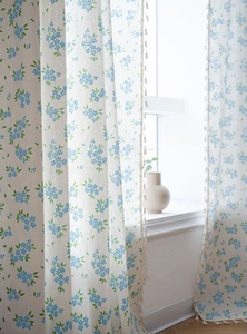 Détail d'un rideau à fleurs bleues avec une bordure décorative de pompons en beige