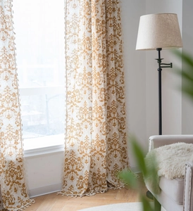 Detail of damascus print curtain fabric with tassel fringe edging in warm beige and gold