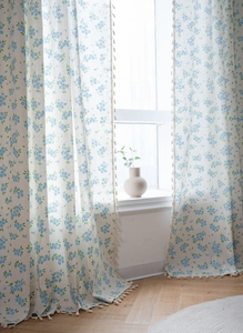 Détail d'un rideau en coton lin à fleurs bleues avec des pompons beiges élégants