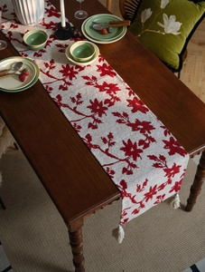 Close-up of beige table runner with red jacquard floral patterns and white fringe edge