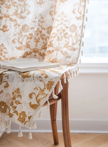 Close-up of khaki floral damask fabric with elegant tassel trim on a wooden chair