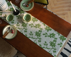 Close-up of jacquard table runner with green leaf patterns on a rustic wooden dining table