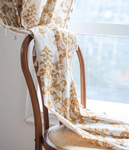 Detail of khaki damask printed curtain with decorative tassels on a vintage wooden chair