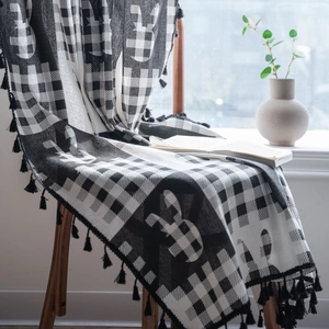 Coperta a scacchi bianchi e neri con motivo a coniglio e nappe su una sedia di legno