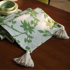 Nordic jacquard table runner with green leaf pattern and tassels on dark wood table