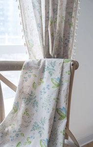 Detailed view of plant print linen curtain fabric with white pom-pom tassel trim edge