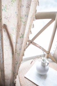 Detailed macro view of beige linen curtains featuring flower embroidery and fringe tassels