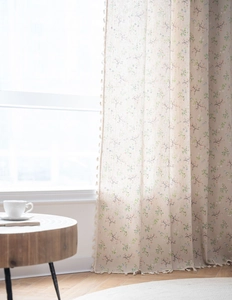 Detailed close-up of floral print linen curtains featuring cream fabric and fringe balls