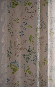 Detailed close-up of linen fabric with green leaf prints and decorative tassels