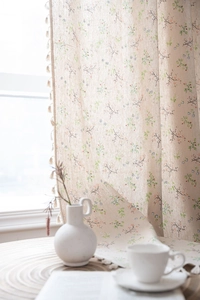 Detail of floral print linen curtains with beige tassel fringe in a bright window setting