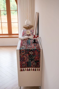 Detail of red geometric jacquard table runner with colorful tassels on a white cabinet