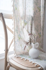 Close-up detail of green leaf printed linen curtains with white tassel trim and fringe