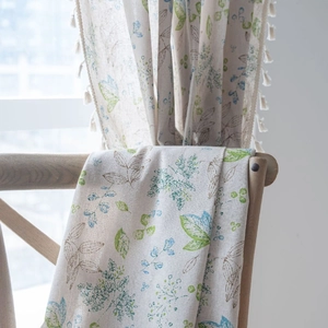 Green leaf and floral print linen curtain with tassel fringe trim on a wooden chair