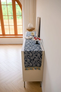 Detailed view of blue woven leaf pattern fabric and elegant tassels on a table runner