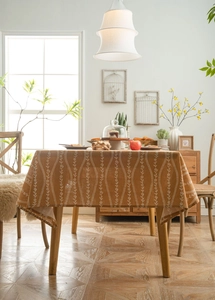 Close-up of ginger yellow cotton linen tablecloth with floral vine patterns on wooden table