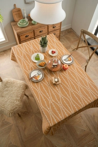 Close-up of orange linen tablecloth with white floral stripes on a wooden dining table
