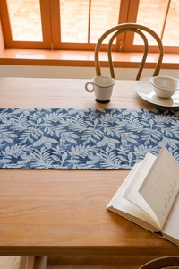 Close-up of blue and white leaf pattern on a textured linen table runner with tassels