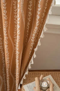 Detail of earthy orange curtain with white floral prints and handmade cream tassels
