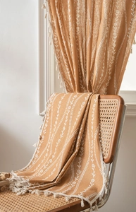 Detail of caramel fabric with white floral embroidery and elegant off-white tassel trim
