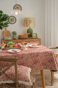 Detail of red floral jacquard tablecloth with matching fringe cushions in a warm dining setting