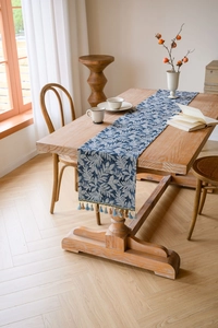 Detail of blue botanical leaf pattern table runner with decorative fringe on wooden table