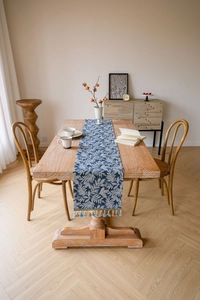 Close-up of blue leaf pattern table runner with elegant tassels on a wooden dining table