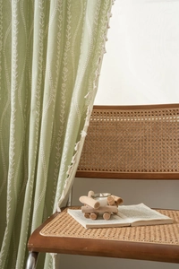 Detail of light green curtains with white floral prints and decorative white tassel edges