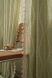 Close-up of green curtain with white wave floral pattern and cream tassel fringe