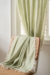 Sage green curtain detail featuring white floral patterns and cream pom-pom fringe trim